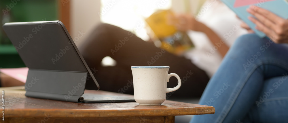 Digital tablet with keyboard and coffee cup on wooden coffee table in living room - obrazy, fototapety, plakaty 