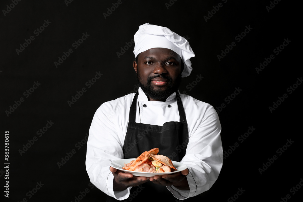 Male African-American chef with tasty dish on dark background Male African-American chef with tasty dish on dark background