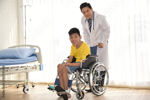 An Asian male Doctor taking care and look after Disabled boy Patient /cripple who can not help himself sitting on wheelchair in hospital/Disability