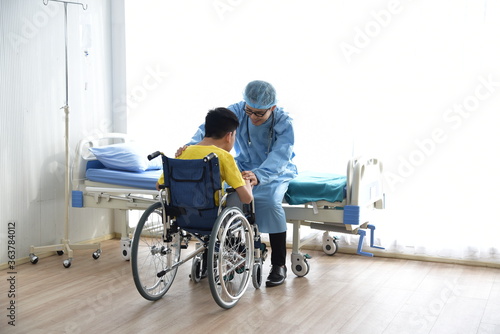 An Asian male Doctor taking care and look after Disabled boy Patient /cripple who can not help himself sitting on wheelchair in hospital/Disability