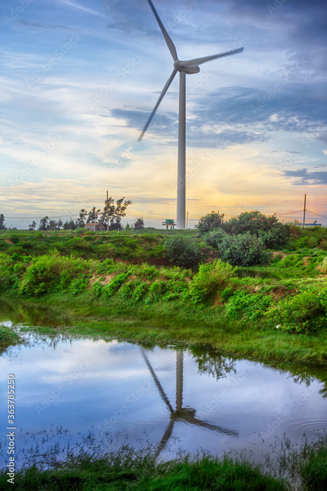 The wind turbine in the evening is reflected in the water.