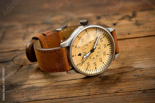 Analog wrist watch with brown dial and brown strap on wooden table