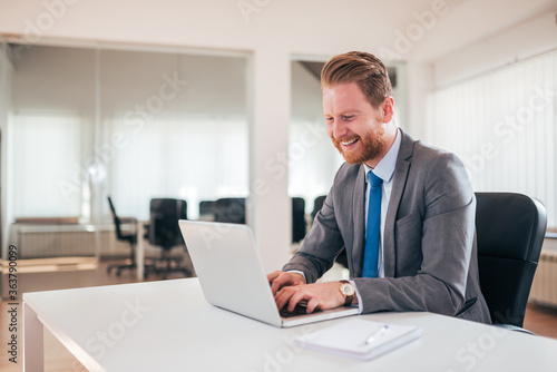 Happy businessman in formalwear typing on laptop in the office.