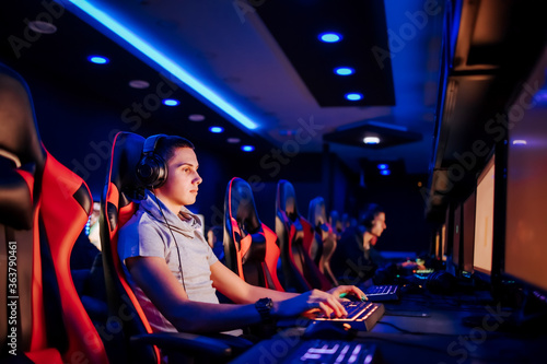 Playing video game on cyber games tournament. Portrait of a teenager with headphones using computer in internet cafe.