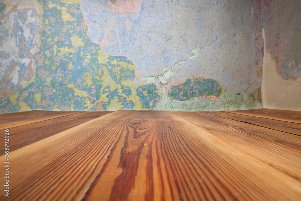 Obraz premium Pusty blat drewnianego stołu zbitego ze starych desek, w tle obdrapana wielokolorowa ściana, pomalowana farbą kredową.