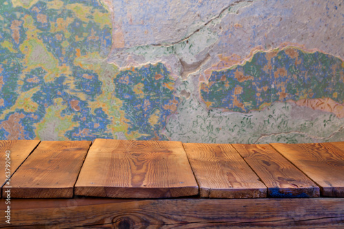 Pusty blat drewnianego stołu zbitego ze starych desek, w tle obdrapana wielokolorowa ściana, pomalowana farbą kredową.