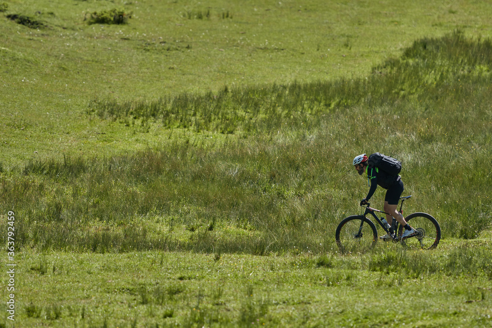 a man on a mountain bike and with a backpack going through a green field