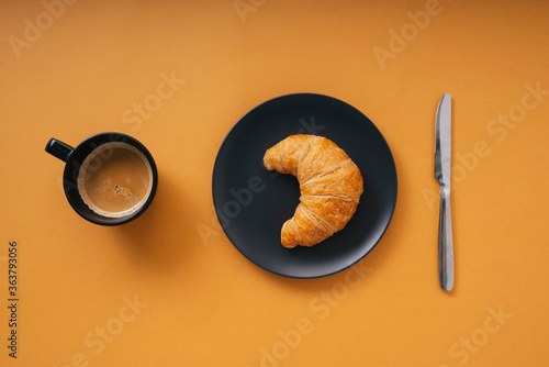 Hot coffee and golden crossiant over orange background. Top view.