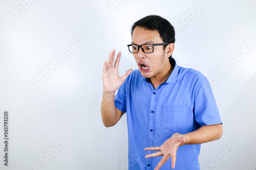 Close up portrait of a young asian man shouting loud and angry facce with arm at his face isolated over white © Reezky