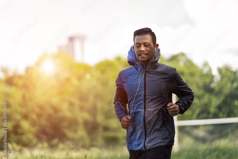 Obraz premium A man in sport hoodie jogging in the city park in the evening after stressful work. Runner jogging training and workout exercising power walking outdoors in forest city. Stock photo