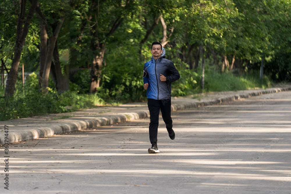 A man in sport hoodie jogging in the city park in the evening after stressful work. Runner jogging training and workout exercising power walking outdoors in forest city. Stock photo A man in sport hoodie jogging in the city park in the evening after stressful work. Runner jogging training and workout exercising power walking outdoors in forest city. Stock photo