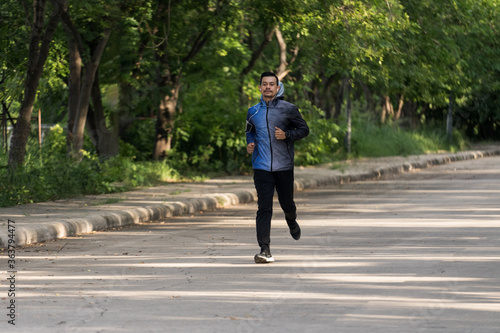 A man in sport hoodie jogging in the city park in the evening after stressful work. Runner jogging training and workout exercising power walking outdoors in forest city. Stock photo