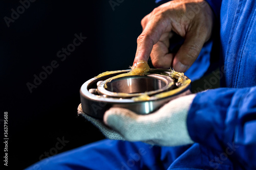 Mechanic is putting lubricant grease into ball bearing in a factory. photo