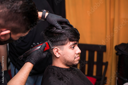 Young hairdresser's hands making haircut to man at barbershop