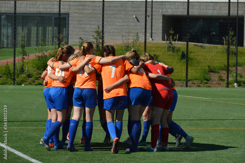 Obraz premium Female football players in orange shirts gathered in circle before the match to raise team spirit and discuss strategy. Selective focus.