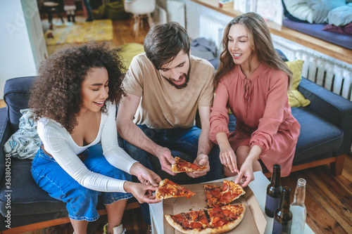 Three young friends taking piece of pizza out of box
