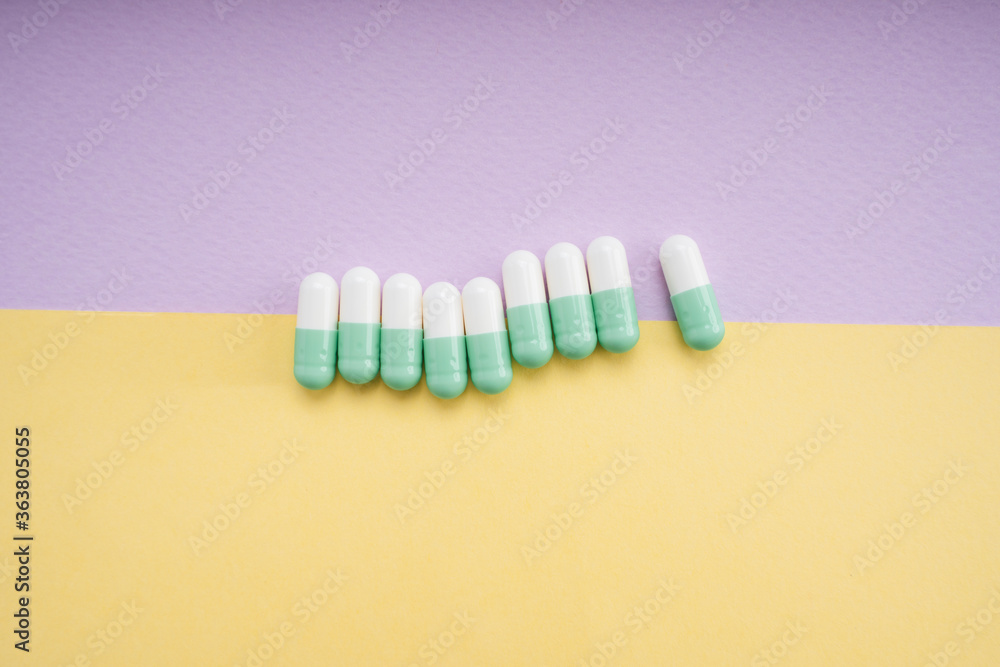White and light green medicine pill capsule over yellow and purple background. White and light green medicine pill capsule over yellow and purple background.
