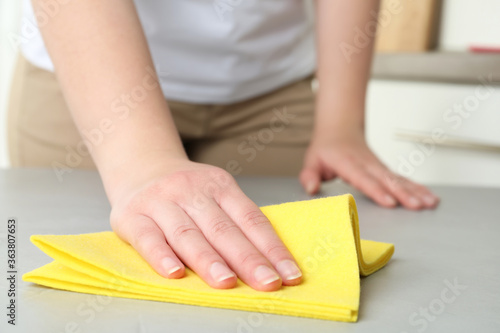 Woman wiping grey table with rag indoors, closeup