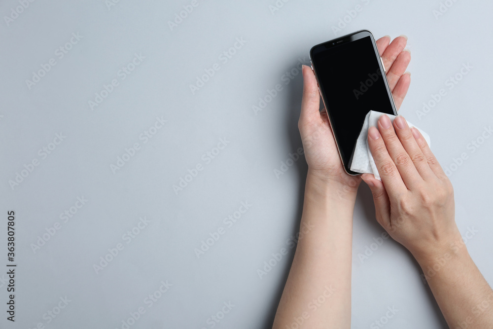 Woman cleaning mobile phone with antiseptic wipe on light grey background, top view. Space for text
