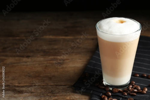 Delicious latte macchiato and coffee beans on wooden table. Space for text
