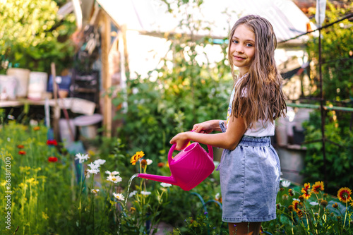 A beautiful gardener a child with a watering can in his hands goes between the beds and water the plants