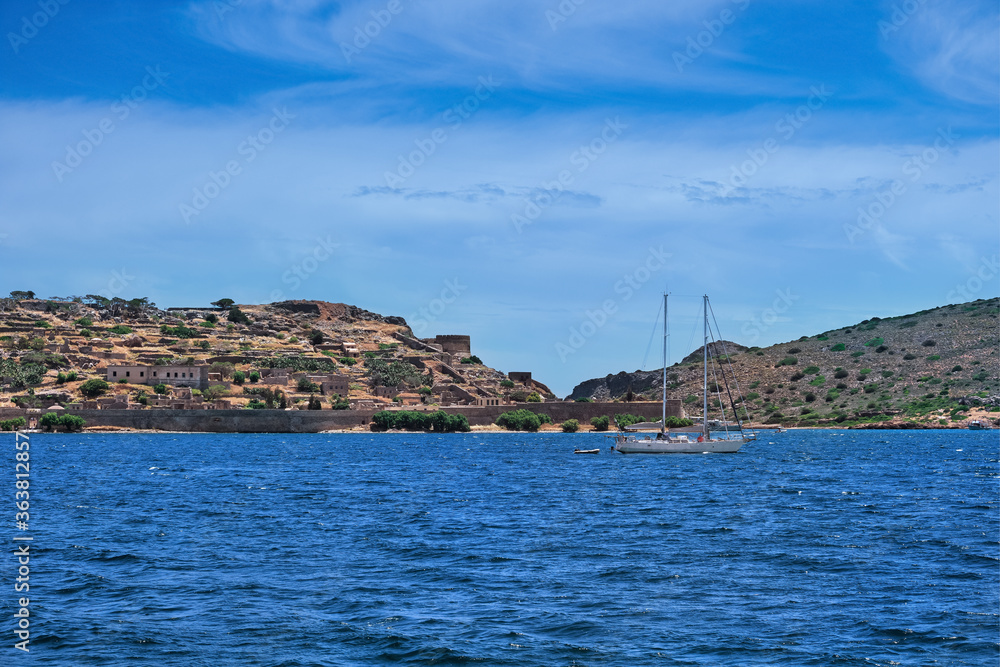 View of Spinalonga island and Venetian fortress, Crete, Greece, and yacht floating on clear summer day