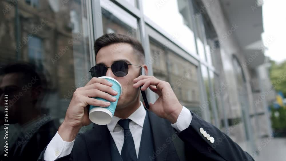 Happy man in sunglasses greets with a hand when talks on smartphone outdoors Happy man in sunglasses greets with a hand when talks on smartphone outdoors