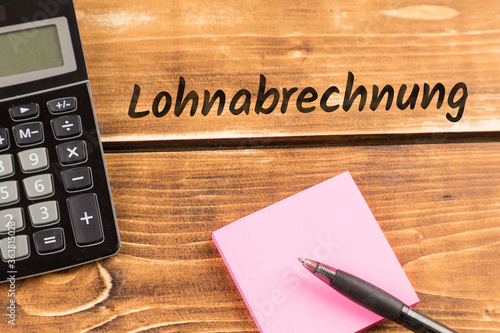 business desk with paper, pen and calculator with german text Lohnabrechnung, in english payroll