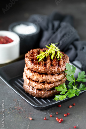 Grilled burger patties with herbs, spices on a dark background