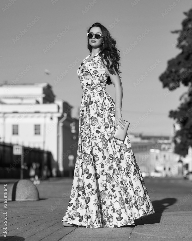Pretty woman with brunette wavy hair. Full length outdoor portrait. Elegant lady in colorful long sundress at street at sunset. Girl walking in the city. Sunny day. Pretty woman with brunette wavy hair. Full length outdoor portrait. Elegant lady in colorful long sundress at street at sunset. Girl walking in the city. Sunny day.
