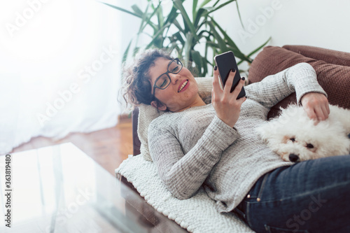 Young woman using mobile phone. Young woman laying on sofa with her dog and using mobile phone.