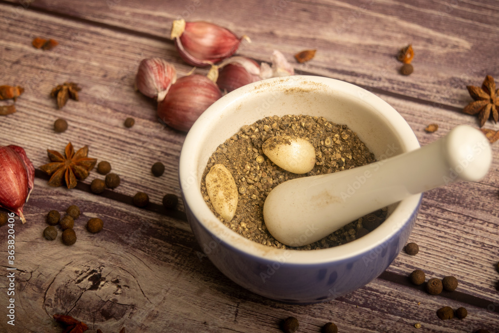 Allspice in a ceramic mortar and scattered garlic cloves, star anise and allspice on a wooden table. Close up. Allspice in a ceramic mortar and scattered garlic cloves, star anise and allspice on a wooden table. Close up.