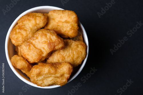 Bucket with delicious chicken nuggets on black background, top view. Space for text