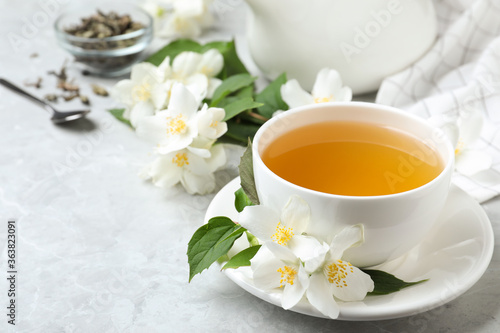 Cup of tea and fresh jasmine flowers on light grey marble table
