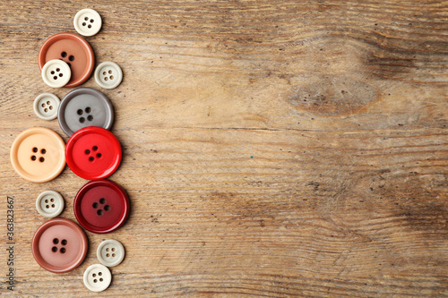 Many plastic sewing buttons on wooden background, flat lay. Space for text