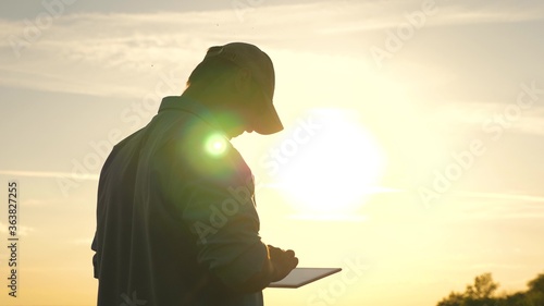 business man working with tablet outdoors. Farmer works with a tablet on a wheat field in the sun. silhouette of an agronomist with tablet studying a wheat crop in a field.
