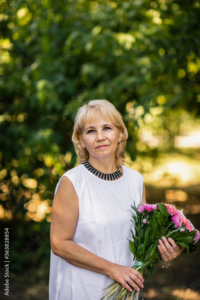 Adult teacher posing with bouquet of pink flowers at the school yard. Green background.
