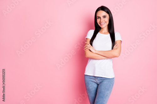 Photo of cheerful pretty young lady hands crossed standing self-confidently showing novelty empty space wear white t-shirt jeans isolated pastel pink color background