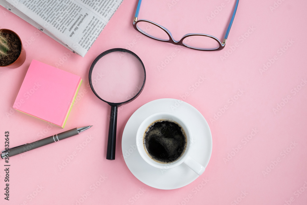 Flat lay on a pink background of coffee cup, glasses, a magnifying glass, cactus, pen and a morning newspaper. Horizontal orientation, selective focus. View from above, copy space.
