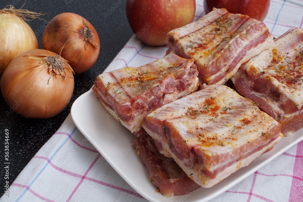 Pork ribs lying on a plate prepared for baking. Onions and apples are the ingredients of the dish