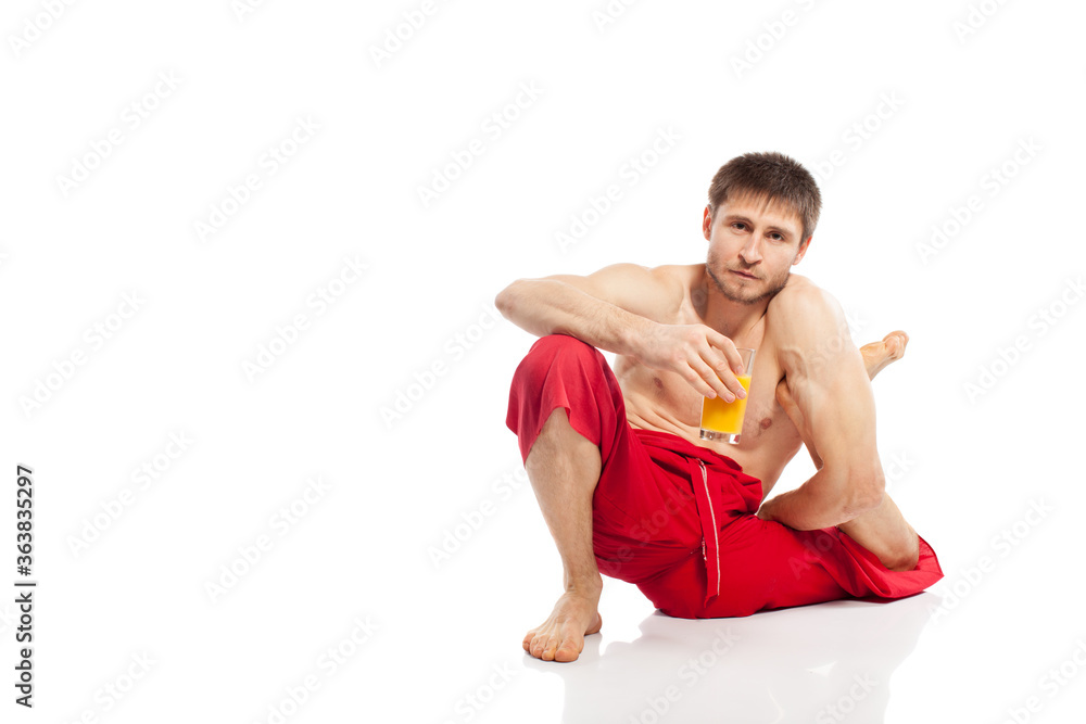 Fototapeta premium Yoga man doing exercises and holding glass with orange juice in studio at white background 