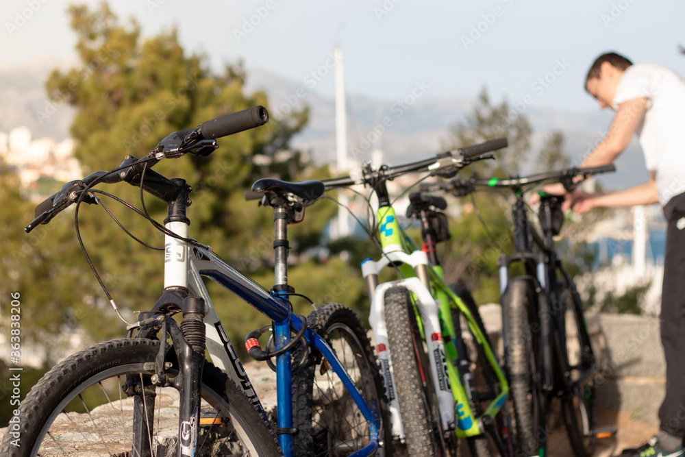 Fototapeta premium Split,Croatia May 2020 Blue green and black mountain bikes standing on a wall. Scott and Cube branded popular bikes, man fiddling with the last bike. Day spend outside in nature