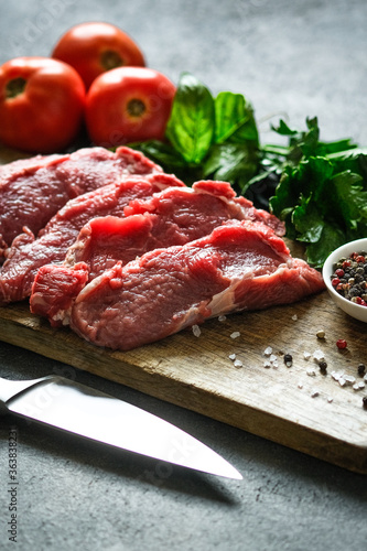 Fresh beef steaks on a board on a dark background with spices and herbs.