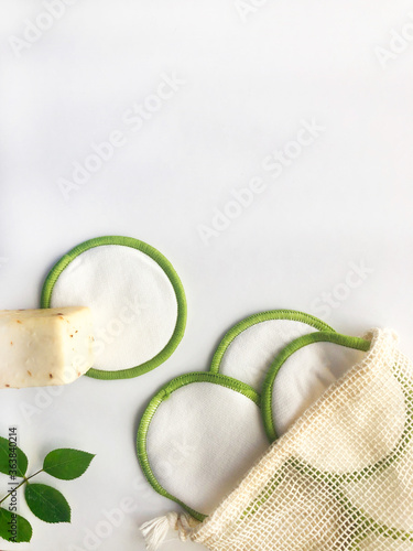 Cosmética belleza natural, ecológica, vegana y reutilizable. Algodones orgánicos, esponja y pastilla de jabón para limpieza facial y corporal. Fondo blanco y madera.