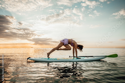 Young woman doing YOGA on a SUP board in the lake at sunrise