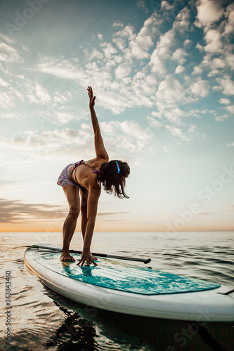 Tablou pe pânză Young woman doing YOGA on a SUP board in the lake at sunrise