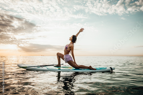 Young woman doing YOGA on a SUP board in the lake at sunrise