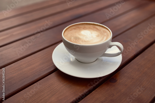 Cup of cappuccino on the wooden background. Beautiful brown foam, white ceramic cup, place for text