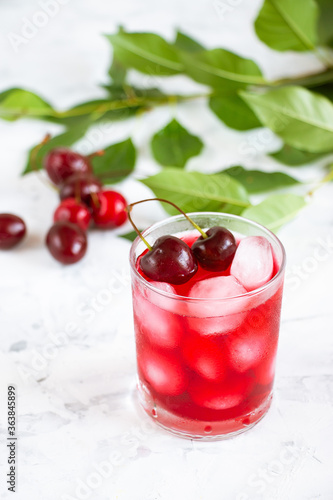 Cherry fruit drink in a glass cup, cherry berries and green leaves on a white background. A refreshing fruit summer drink.