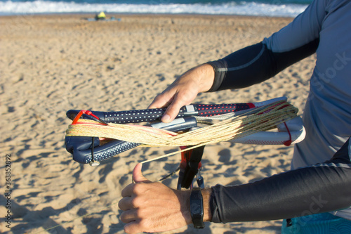 Fotografie close up a man hands rolling a kite bar and lines on the beach after kitesurfing with sea on background